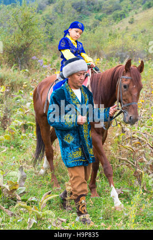 Balades autour de l'homme kazakh avec son fils sur un cheval après la cérémonie de circoncision Sundet Toi, Kazakh village ethnographique Banque D'Images