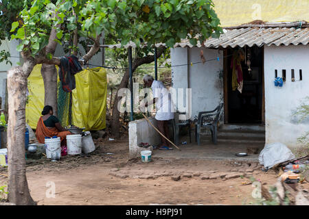 Old Indian man nettoie après le nettoyage de ses dents alors que sa femme fait la lessive à l'extérieur de leur maison à Chennai Banque D'Images