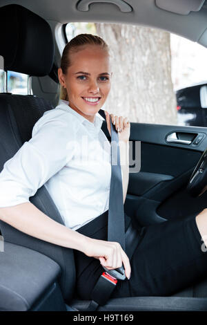 Smiling blonde business woman sitting in car et de mettre sur la ceinture de son Banque D'Images