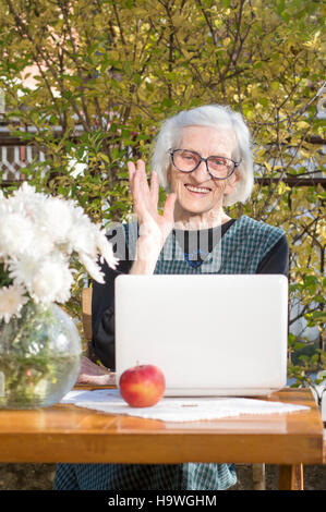 Femme de 90 ans tout en ayant un signe un appel vidéo sur un ordinateur portable blanc Banque D'Images