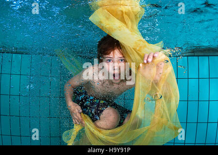 Surpris jeune garçon jouant sous l'eau dans une piscine avec un chiffon jaune entourée par des bulles Banque D'Images