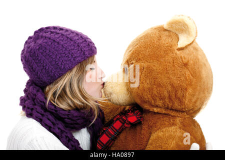 Jeune femme portant un chapeau en laine mauve et foulard embrassant un ours en peluche Banque D'Images