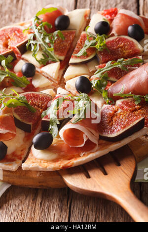 Découpé une pizza aux figues, jambon et mozzarella gros plan sur une planche en bois vertical. Banque D'Images