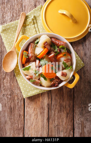 Un plat traditionnel irlandais est dorloter avec des saucisses de porc, le bacon et les légumes dans un pot jaune sur la table. vertical Vue de dessus Banque D'Images