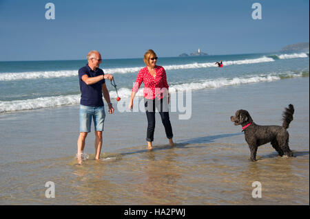 Un couple (mâle et femelle) de porter des vêtements d'été avec leur chien s'amusant sur une plage ensoleillée Cornish. Banque D'Images