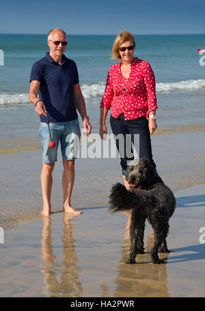 Un couple (mâle et femelle) de porter des vêtements d'été avec leur chien s'amusant sur une plage ensoleillée Cornish. Banque D'Images