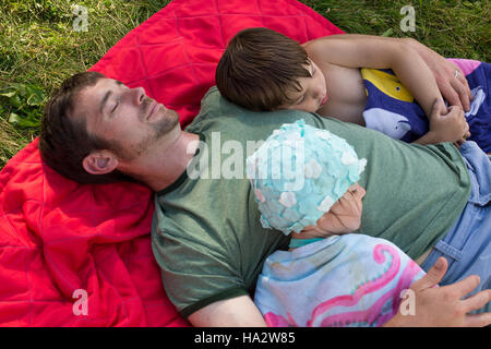 Son père et ses deux enfants dormant on picnic blanket Banque D'Images