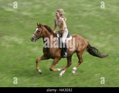 Cavalière à cheval galopant à travers un pré vert Banque D'Images
