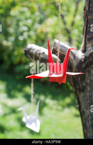 En origami dans le jardin. Les figures de papier dans la nature. Les grues rouges et blanches sur arbre.