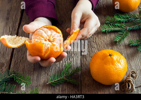 La mandarine et branches de sapin dans les mains des enfants close up sur fond de bois rustique - se préparer à l'époque de Noël et vacances d'hiver à home concept Banque D'Images