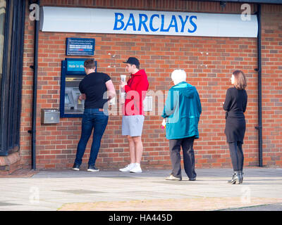 Quatre clients faisant la queue pour utiliser un distributeur automatique de billets ou à une succursale de la banque Barclays Banque D'Images