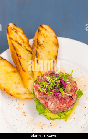 Tartare de thon ahi empilé avec avocat, roquette, garnie de pousses, servi avec du pain grillé crostini Banque D'Images