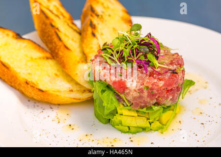 Tartare de thon ahi empilé avec avocat, roquette, garnie de pousses, servi avec du pain grillé crostini Banque D'Images