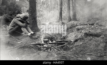 Jeune femme assise seule dans la forêt par le feu Banque D'Images