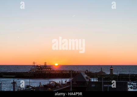 Le lever du soleil sur la mer avec le port de Ramsgate et bureaux phare sur mur du port en premier plan. Mince bande de ciel orange sur l'horizon avec lever de soleil. Banque D'Images