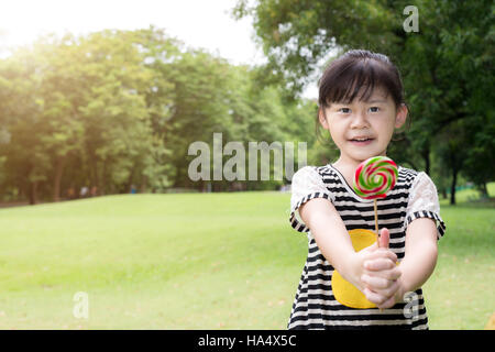 Asian little girl eating lollipop extérieur dans spring park Banque D'Images