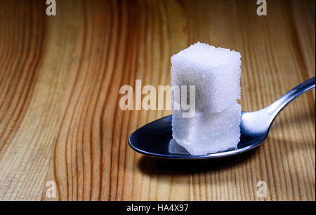 Deux cuillère de sucre morceaux reposant sur une cuillère à café d'argent sur un fond texturé en bois. Banque D'Images