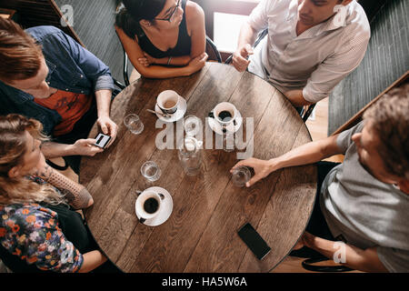 Vue supérieure de jeunes gens assis au café avec une tasse de café sur la table. Groupe d'amis au café. Banque D'Images