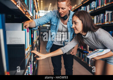 Les jeunes étudiants à trouver des ouvrages de référence en bibliothèque universitaire. L'homme et la femme recherche d'informations pour leurs études. Banque D'Images