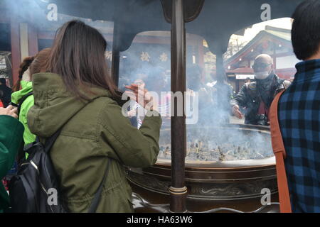 Tokyo, Japon-2/28/16: Une femme en vert (avec d'autres) se rassemble autour du jokoro du temple Sensoji d'Asakusa pour y faire passer la fumée de l'encens. Banque D'Images