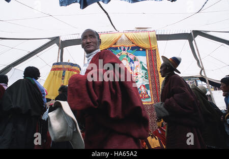 Légende : Axu, Sichuan, Chine - 19 août 2003. Un peuple nomade khampa homme, son chapeau dans le respect, marche devant un thanka bouddhiste (peinture) pendant le festival o Banque D'Images