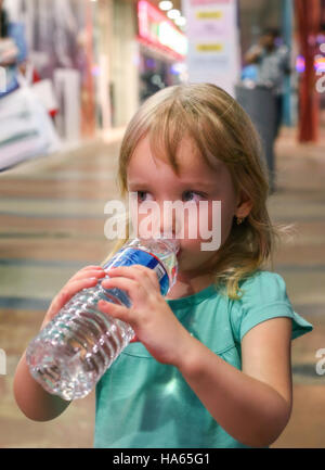 Petite fille boit de l'eau d'une grande bouteille. Banque D'Images