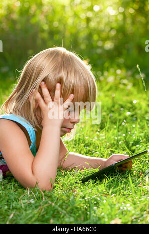 Petite fille à l'aide d'une tablette tactile dans un jardin d'été Banque D'Images