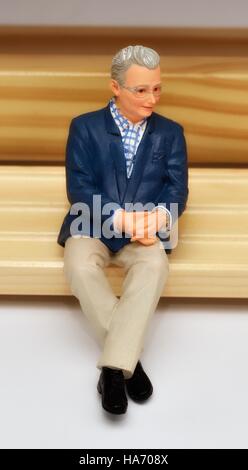 Un homme âgé retraité senior figurine miniature assis sur un banc en bois. Banque D'Images