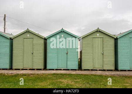 Une rangée de cabanes de plage assis sur le bord supérieur de la plage sont protégés avec un mélange de peinture naturellement avec les défenses côtières Banque D'Images