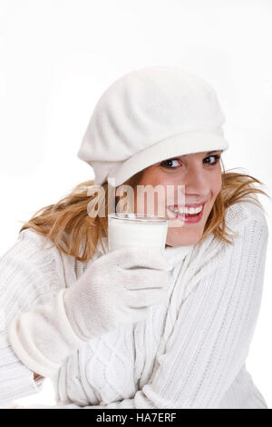 Jeune femme dans un chandail à col roulé blanc avec bonnet de laine tenant un verre de lait Banque D'Images