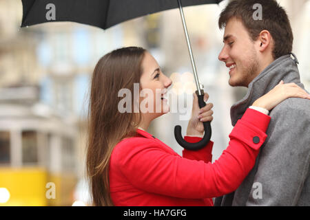 Vue latérale d'un couple de rencontrer dans la rue sous un parapluie un jour de pluie Banque D'Images