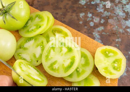 Trancher les tomates à la main verte sur une planche à découper en bois Banque D'Images