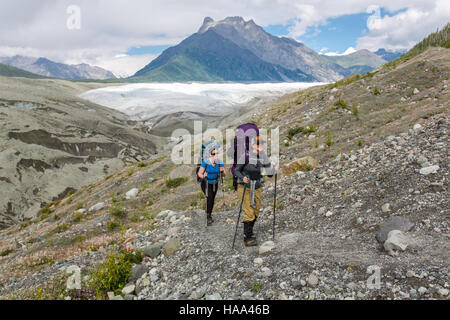 Deux randonneurs sont photographiés sur le sentier Root Glacier Trail en Alaska, un itinéraire populaire pour les randonneurs qui cherchent à découvrir la nature sauvage vierge de l'Alaska et les magnifiques paysages glaciaires dans un cadre de parc national. Banque D'Images