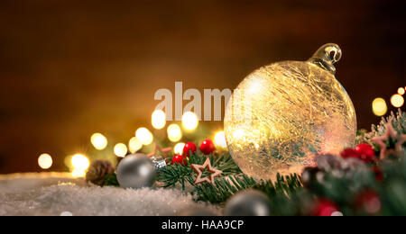 Libre d'une boule de noël transparente, branches de sapin et des ornements sur la neige, avec les feux de flou artistique et de l'espace de copie sur le bois à l'arrière-plan Banque D'Images