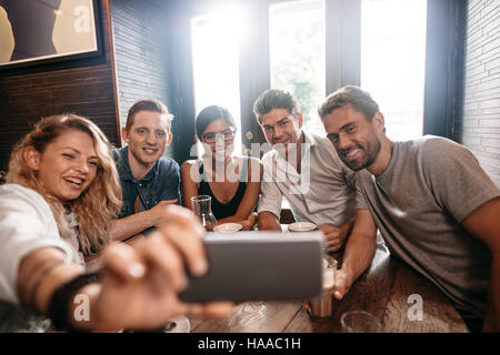 Petit groupe d'amis en tenant sur un selfies téléphone mobile. Les jeunes hommes et les femmes siégeant ensemble au café et prendre un autoportrait sur téléphone intelligent. Banque D'Images