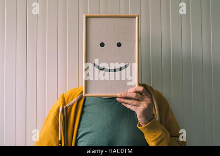 Mettre un visage heureux, sur le bonheur et les émotions gaies concept, man holding photo frame avec imprimé émoticône smiley Banque D'Images