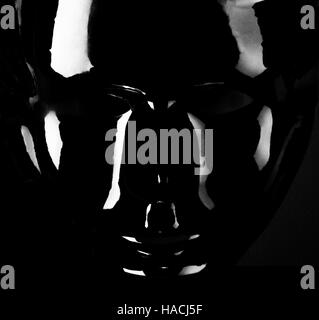 Silhouette masque noir brillant sur fond noir. Banque D'Images