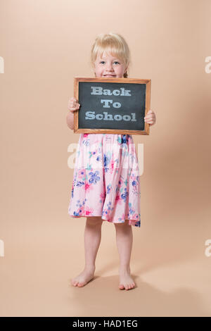 Petite fille d'âge scolaire holding tableau avec 'Back to School' message Banque D'Images