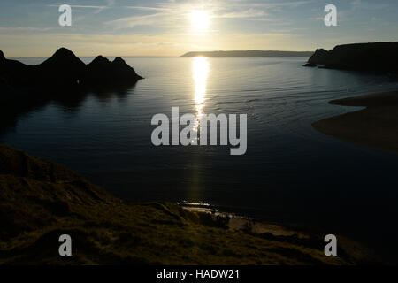 Trois falaises bay, Gower, le Pays de Galles au coucher du soleil . Une marée haute remplit la vallée avec la lumière se reflétant le Ciel clair Ciel du soir. Banque D'Images