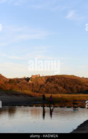 Un couple avec leur chien traverser le stepping stones à trois falaises bay, Gower, le Pays de Galles au coucher du soleil . Banque D'Images