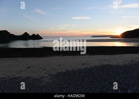 Trois falaises bay, Gower, le Pays de Galles au coucher du soleil . Une marée haute remplit la vallée avec la lumière se reflétant le Ciel clair Ciel du soir. Banque D'Images