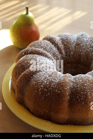 Un gâteau poire saupoudrés de sucre en poudre est vu sur une plaque prête à couper et servir avec une poire en arrière-plan. Banque D'Images