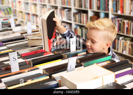 Petit étudiant dans la bibliothèque. Le garçon choisit un livre Banque D'Images