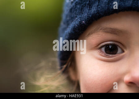 Jeune fille au chapeau en laine bleu chaud. La moitié des enfants en face d'hiver wooly hat souriante avec des yeux seulement dans le châssis entièrement Banque D'Images