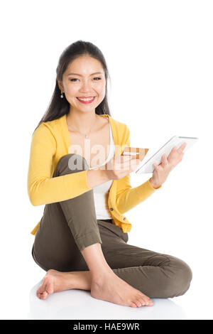 Portrait de femme asiatique décontractée assis sur plancher à l'aide d'un écran tactile tablet pc pour le magasinage en ligne et effectuer le paiement, isolé sur blanc bac Banque D'Images