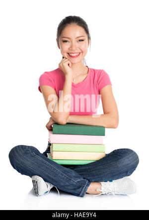 Jeune asiatique de tout le corps étudiant college girl in pink shirt avec pile de manuels scolaires, assis sur le plancher, pleine longueur isolé sur fond blanc. Banque D'Images