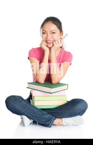 Full body girl in pink shirt avec les manuels scolaires, assis sur le plancher, pleine longueur isolé sur fond blanc. Banque D'Images