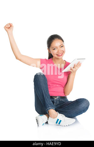 Full body girl in pink shirt using digital tablet computer et acclamer, assis sur le plancher, pleine longueur isolé sur fond blanc. Banque D'Images