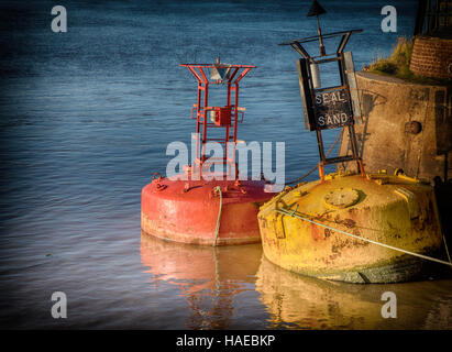 Deux vieilles bouées, la mer rouge et jaune, flottant dans l'eau et lié à la mur du port. L'un a une plaque disant sable joint Banque D'Images