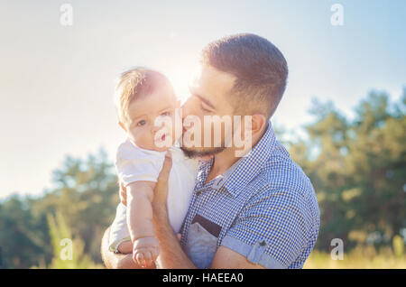 Jeune papa embrasser un bébé. Soir d'automne à pied à l'extérieur. Éruption solaire illumine le bébé et papa. Banque D'Images